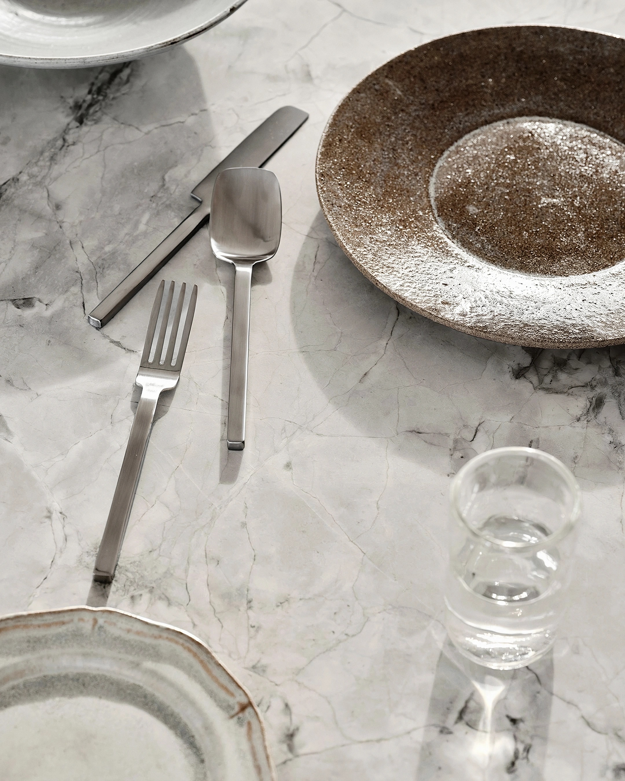Place setting on marble at Elena House, with ceramic plates, silver cutlery and a glass